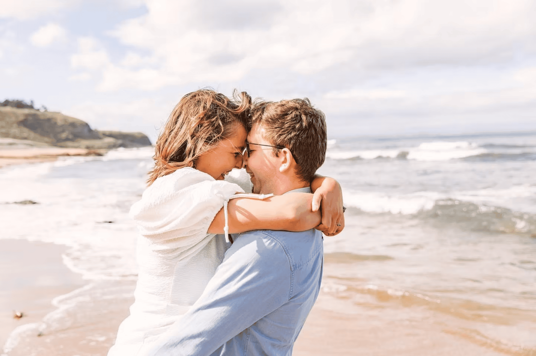 Couple embracing and laughing together on a sunny coastal beach